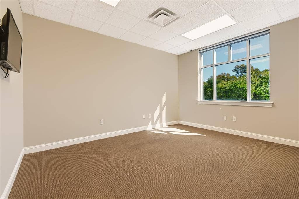 3900 S Stonebridge Drive, #203, McKinney, TX 75070 Carpeted flooring, expansive windows, drop ceiling with integrated lighting, wall-mounted television bracket, and neutral-toned walls
