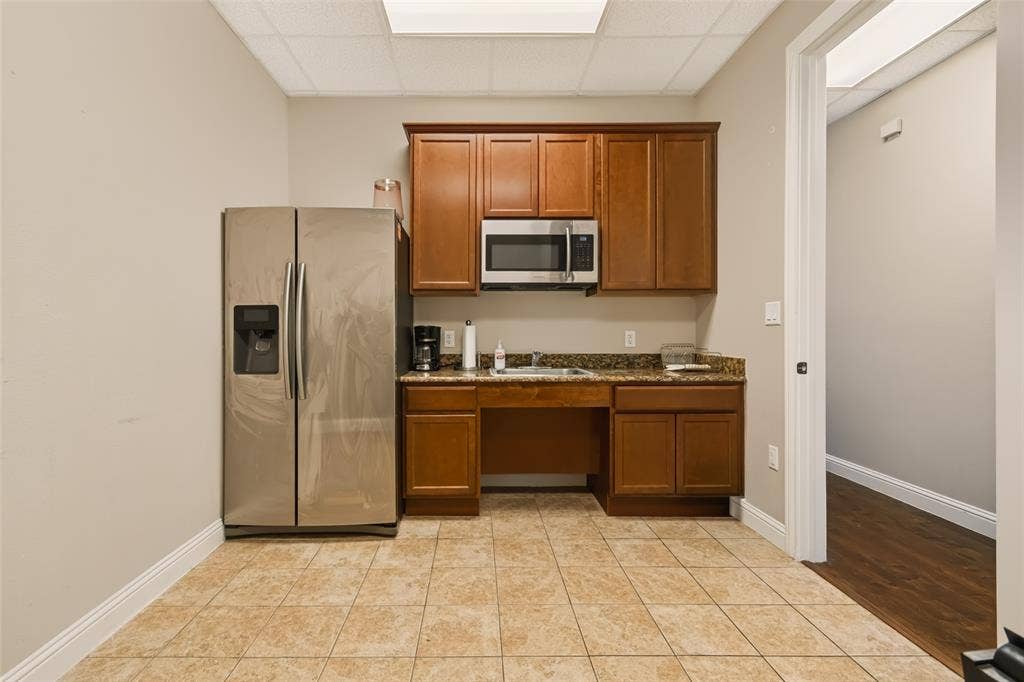 3900 S Stonebridge Drive, #203, McKinney, TX 75070 Kitchenette featuring wood cabinetry, stainless steel microwave, stone-finish countertops, and tile flooring