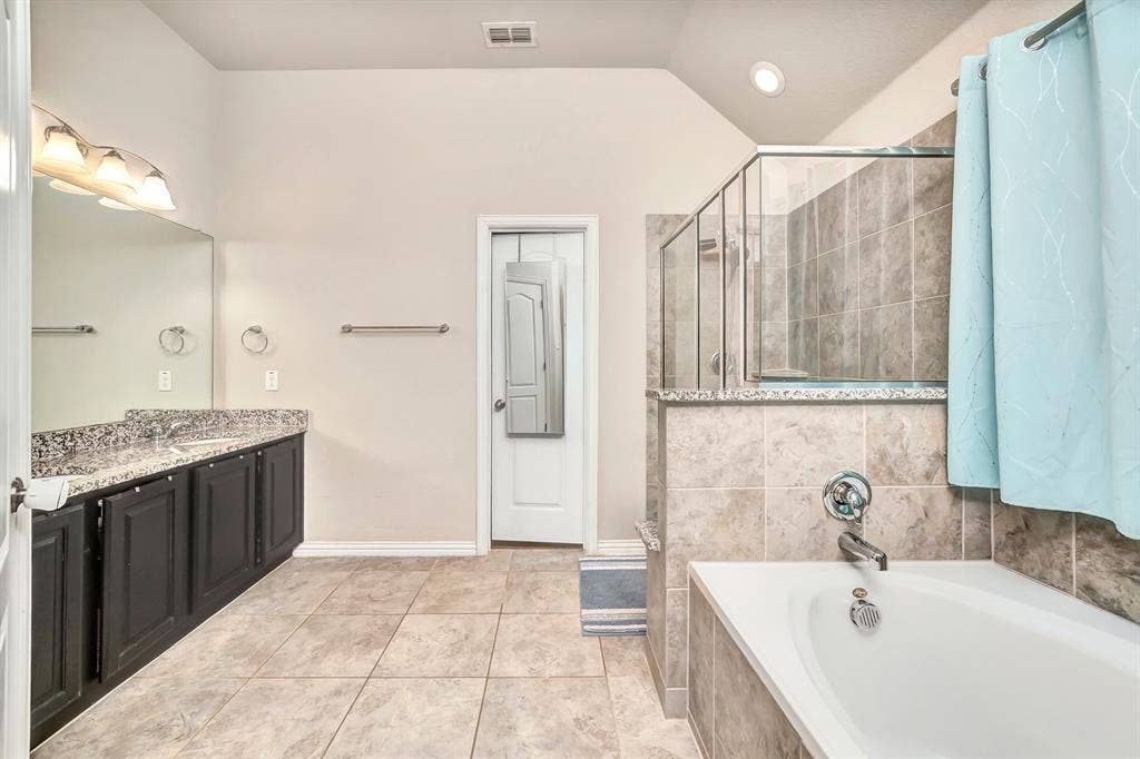 Bathroom featuring dark cabinetry with a stone-finish countertop, a deep soaking tub, and a separate glass-enclosed shower with tile surround