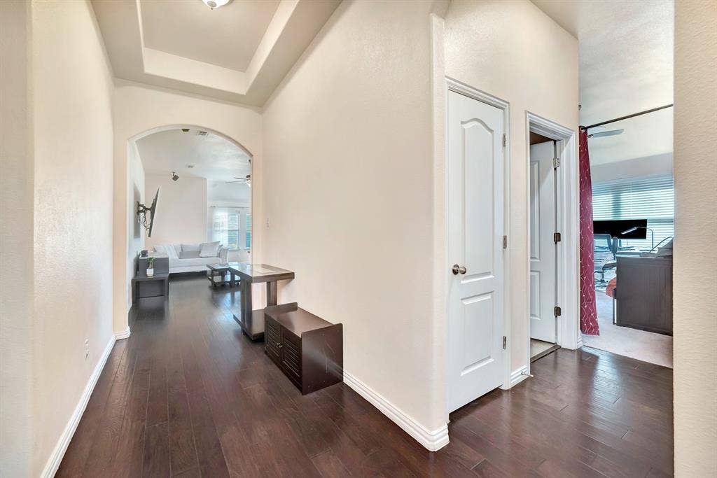 Interior hallway featuring wood-finish flooring, a tray ceiling, an arched entryway, and six-panel interior doors