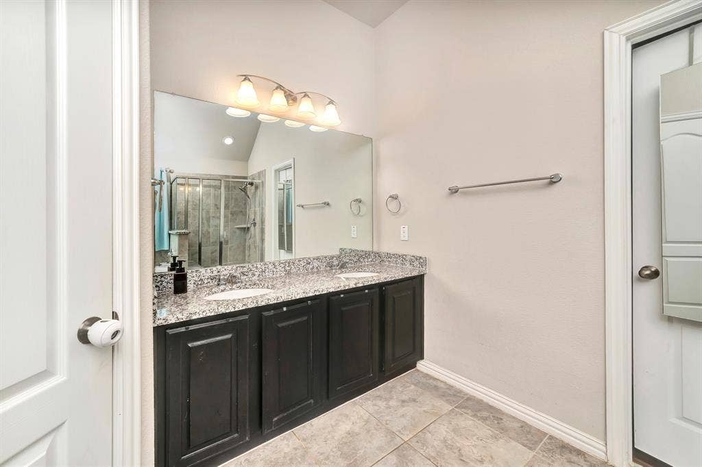 Dual-vanity cabinet with dark-finish cabinetry, stone-patterned countertop, under-mount sinks, large wall-mounted vanity mirror, and multi-bulb light fixture