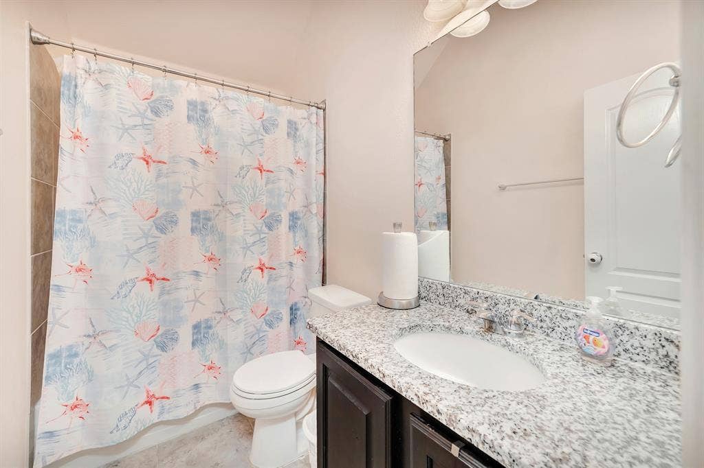 Full-height wall mirror, stone-finish countertop with integrated sink, dark wood-finish cabinetry, and tiled shower enclosure