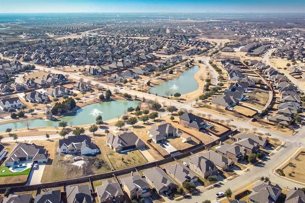 Aerial perspective of a suburban neighborhood featuring multiple retention ponds, decorative water fountains, paved street infrastructure, and residential structures with shingled roofing