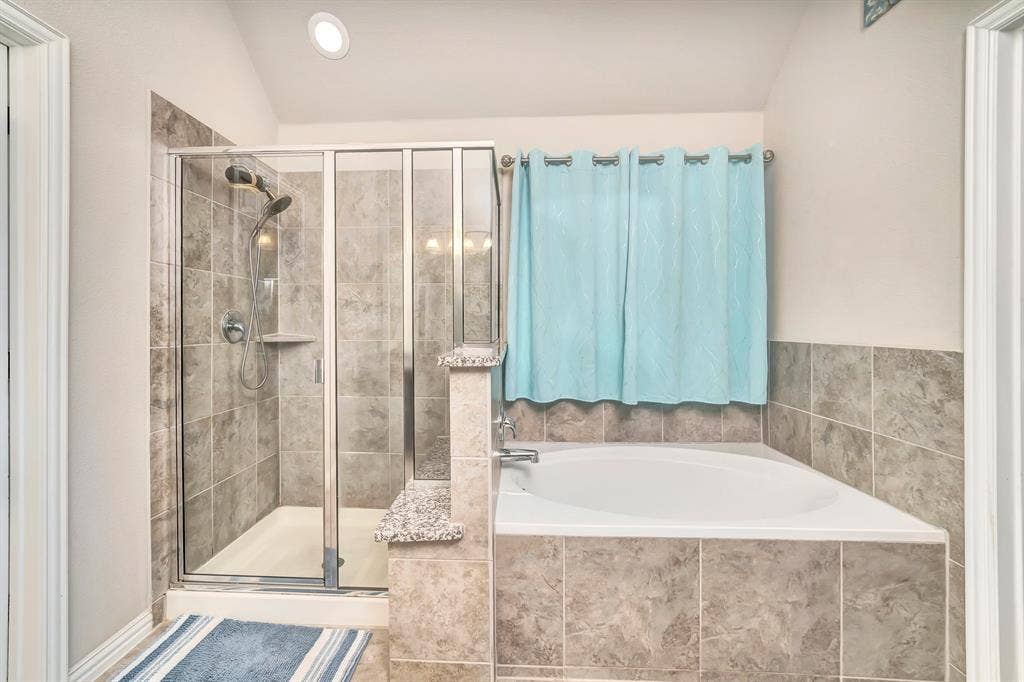 Bathroom featuring a glass-enclosed shower, a deep soaking tub with tile surround, stone-finish countertops, and vaulted ceilings with recessed lighting