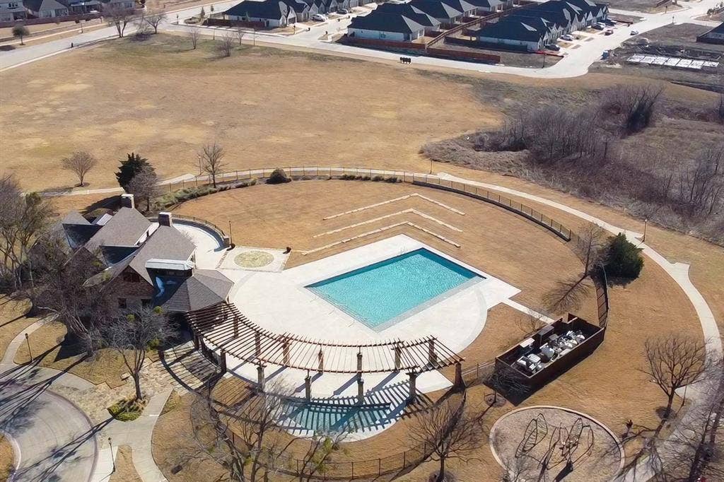 Expansive grounds featuring a swimming pool with concrete decking, a curved wooden pergola, integrated stone landscaping features, and a permanent metal-fenced enclosure