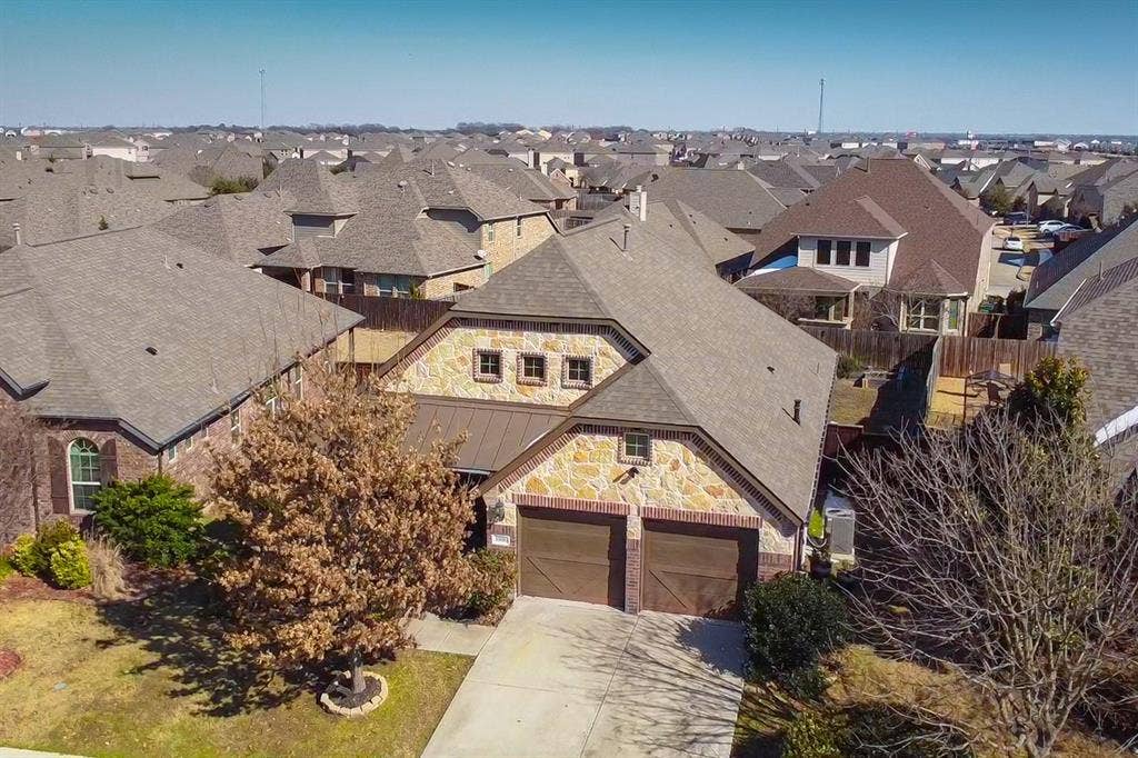 Aerial view of property featuring a stone facade, dual-bay garage, concrete driveway, and asphalt shingle roofing