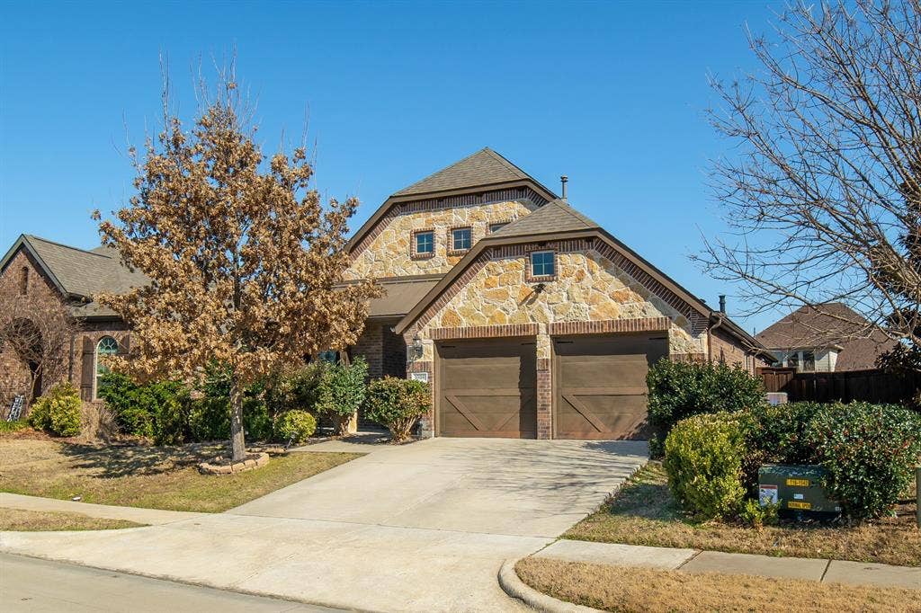 Exterior featuring stone masonry facade, dual carriage-style garage doors, multi-gabled roofline, and concrete driveway