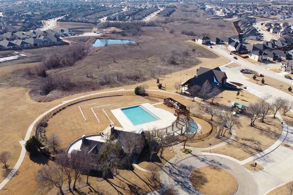 Aerial perspective featuring a rectangular swimming pool, expansive hardscaped patio, integrated wood-finish pergola, and fenced perimeter