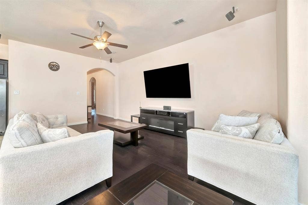 Living area featuring wood-finish flooring, a ceiling fan with integrated light, and an arched doorway