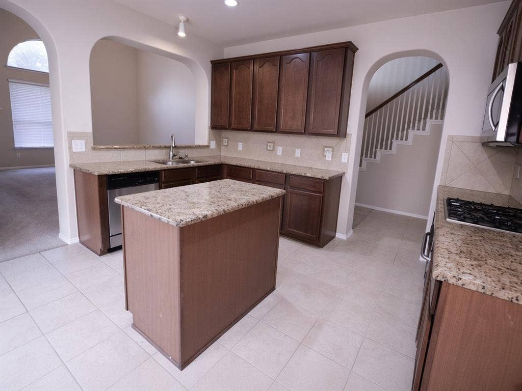11398 Seguin Drive, Frisco, TX 75035 Kitchen featuring a central island, granite countertops, wood cabinetry, stainless steel appliances, and tile flooring