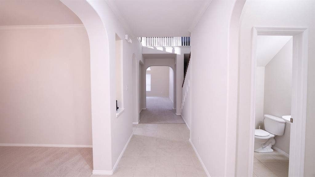 11398 Seguin Drive, Frisco, TX 75035 Arched doorways, tile flooring, carpeted room, carpeted stairway with white balusters, and a powder room with a commode and pedestal sink