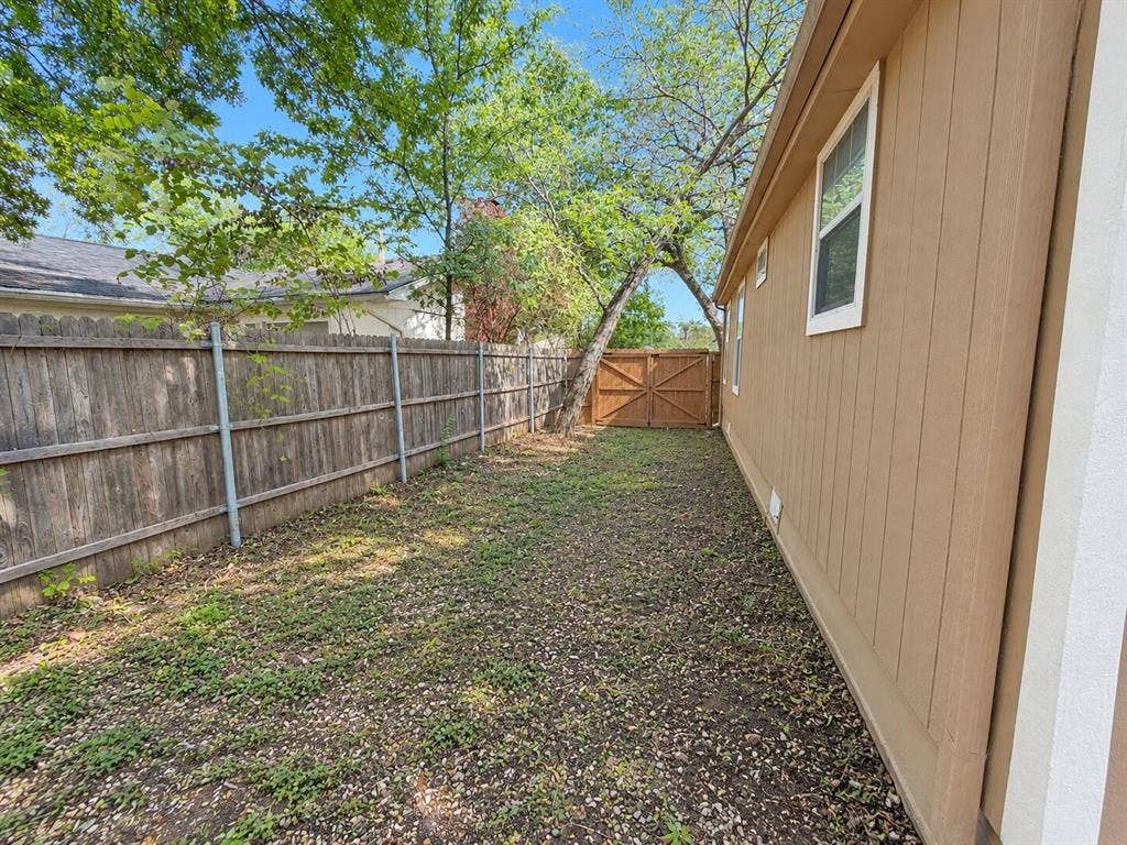 Fenced yard with a wooden privacy fence, mature trees, and a side access gate