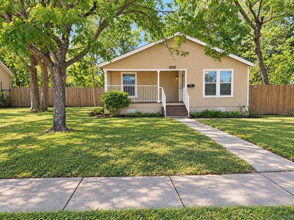 Neutral-toned exterior with a covered porch, white railing, and a wood privacy fence