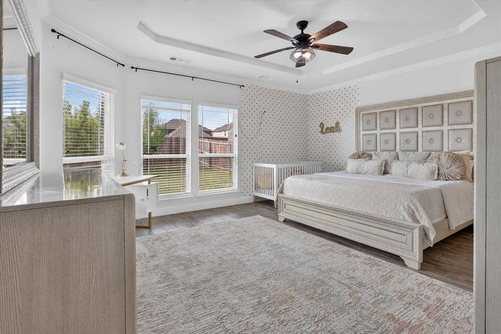 Tray ceiling with a ceiling fan, wood-finish flooring, and multiple windows providing natural illumination