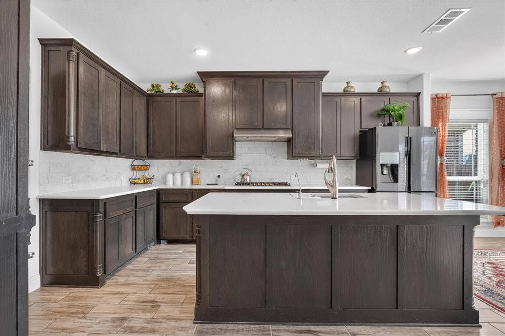 Expansive kitchen featuring dark wood cabinetry, white countertops, a subway tile backsplash, and wood-finish flooring