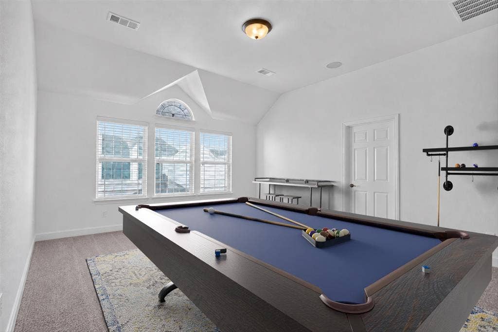 This room has been virtually staged with a pool table. Vaulted ceiling, arched transom window, three rectangular windows, paneled interior door, and ceiling-mounted light fixture