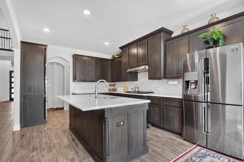 Kitchen featuring dark wood-finish cabinetry, white countertops, white subway tile backsplash, a stainless steel refrigerator, and wood-finish flooring