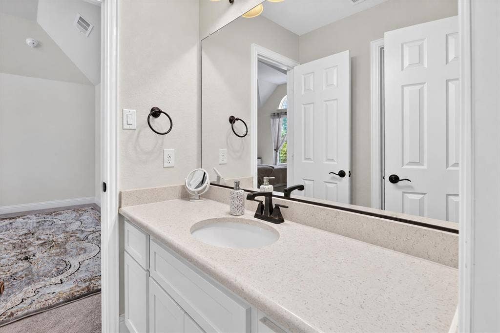 White vanity with an integrated sink, light-toned countertop, large wall mirror, and dark-finished faucet