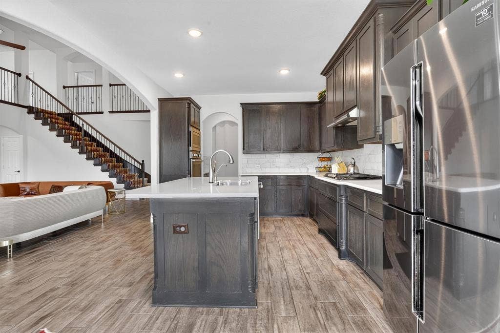 Gourmet kitchen with dark wood-finish cabinetry, stainless steel appliances, a center island with sink, and wood-finish flooring