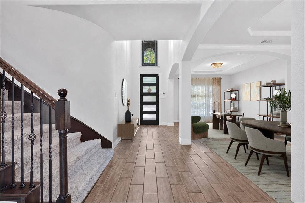 Wood-finish tile flooring throughout the entry, staircase with wood handrails and wrought iron balusters, arched hallway openings, and recessed lighting. The furniture has been virturally staged.