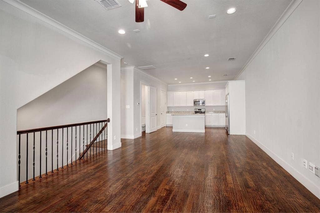 Wood-finish flooring, white walls, recessed lighting, and a white kitchen with stainless steel appliances