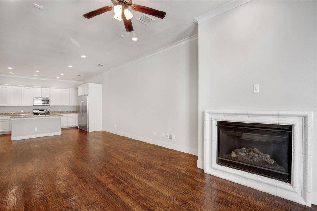Living area featuring wood-finish flooring, a ceiling fan, crown molding, and a tiled fireplace