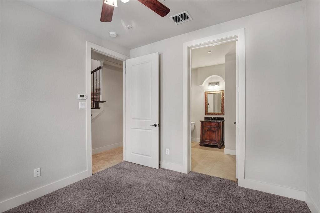 Carpeted room with a ceiling fan, white paneled door, and access to a bathroom featuring a wood-finish vanity and tiled flooring