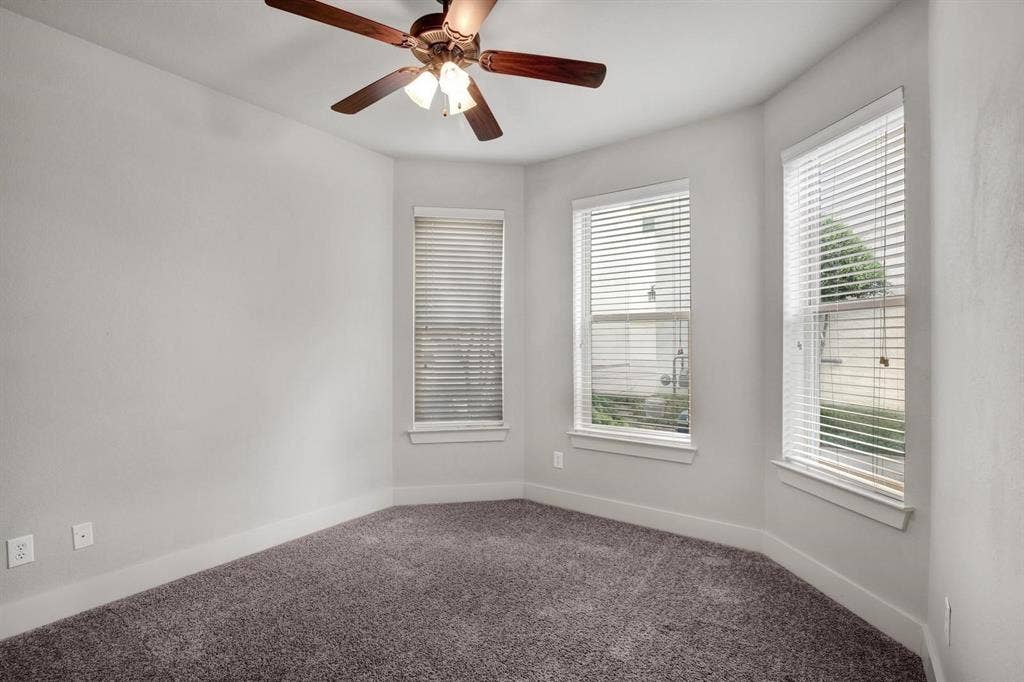 Neutral wall color, textured carpet, multiple windows with blinds, and a ceiling fan with integrated lighting