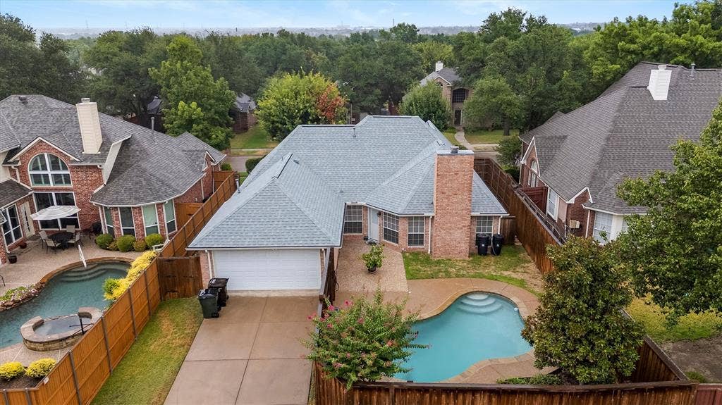 3916 Montrose Drive, Plano, TX 75025 Elegant brick residence featuring a light-colored tile roof, expansive driveway with concrete paving, and resort-style backyard with sparkling swimming pool and spa