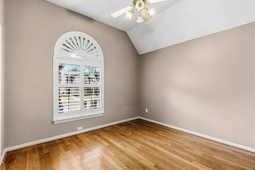 3916 Montrose Drive, Plano, TX 75025 Bright upper-level bedroom featuring warm wood-finish flooring, neutral taupe walls, and an arched transom window with plantation shutters