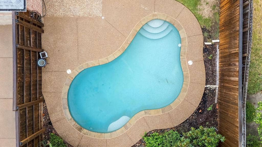 3916 Montrose Drive, Plano, TX 75025 Pear-shaped swimming pool with integrated steps, surrounded by an aggregate concrete patio and perimeter landscaping