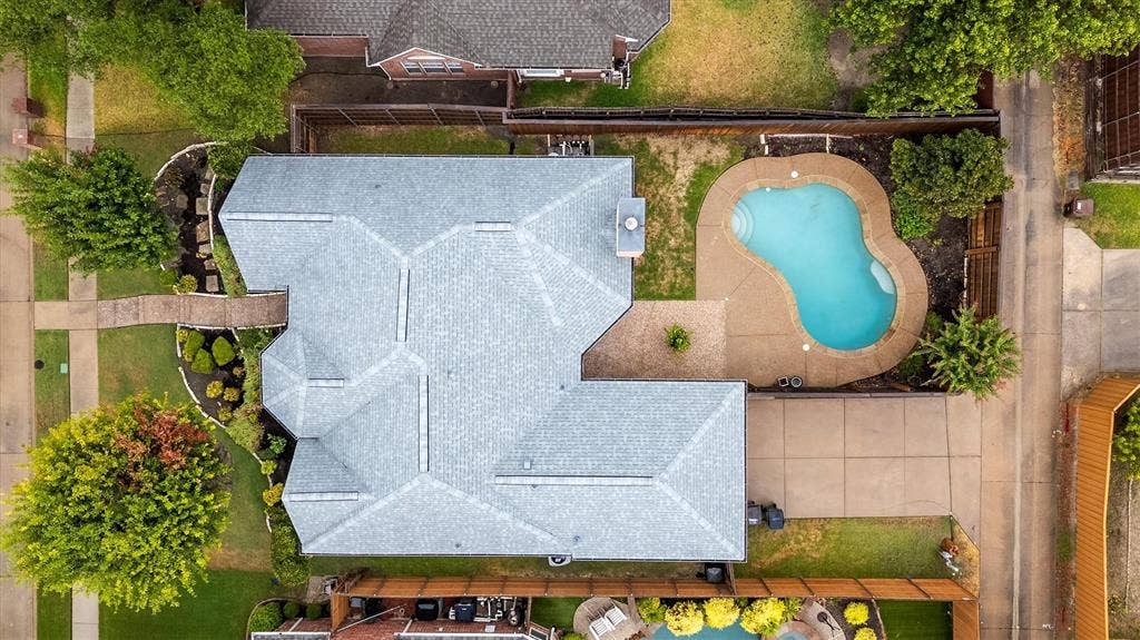 3916 Montrose Drive, Plano, TX 75025 Aerial view showcasing a light-colored roof with geometric paneling, resort-style free-form swimming pool with sun deck, mature landscaping throughout the property, and expansive hardscaped entertaining areas adjacent to lush green spaces
