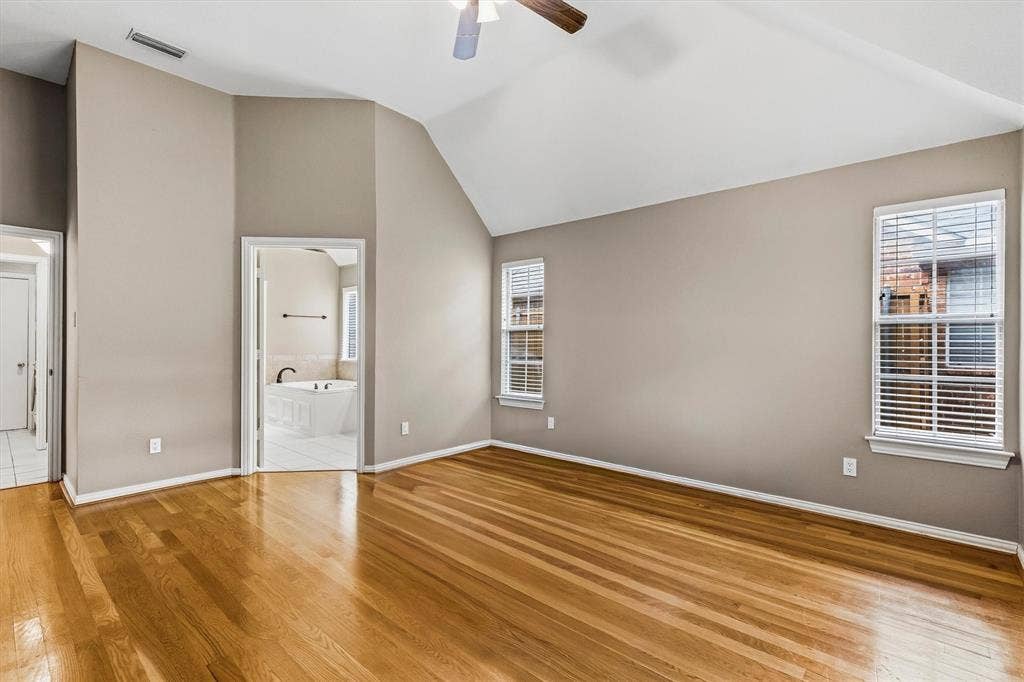 3916 Montrose Drive, Plano, TX 75025 Vaulted ceiling, wood-finish flooring, two windows with blinds, ceiling fan, and access to an adjoining bathroom with a built-in tub