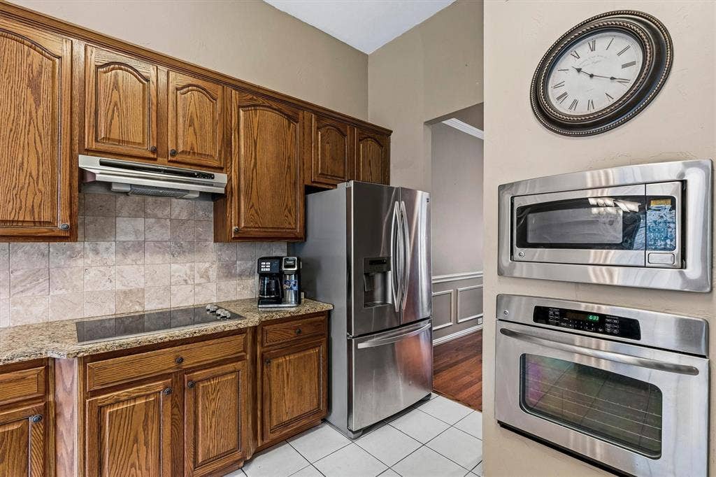 3916 Montrose Drive, Plano, TX 75025 Wood cabinetry, granite-finish countertop, tile backsplash, built-in cooktop, and stainless steel appliances