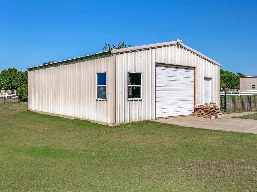 508 Singing Quail Trail, Haslet, TX 76052 Metal-sided structure with a pitched roof, two windows, a white roll-up garage door, and a single entry door