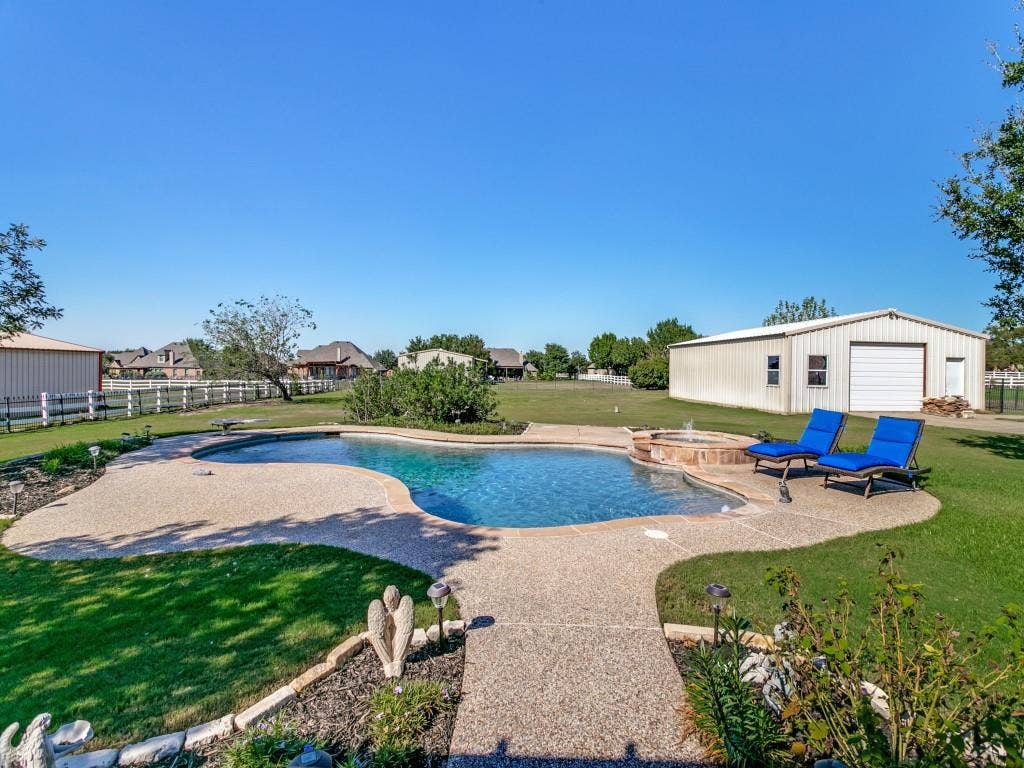 508 Singing Quail Trail, Haslet, TX 76052 Freeform swimming pool with an integrated spa, expansive concrete pool deck, and a detached metal building with a garage door