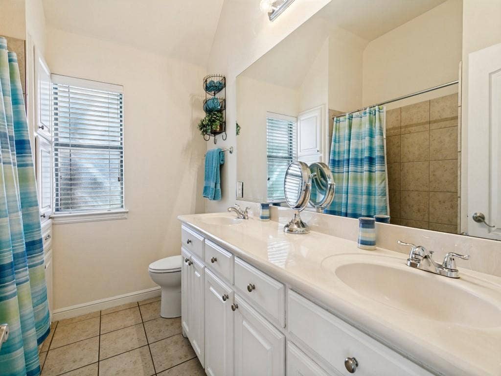 508 Singing Quail Trail, Haslet, TX 76052 Dual sink vanity with white cabinetry and chrome hardware, a large mirror, a separate toilet area, and tiled flooring