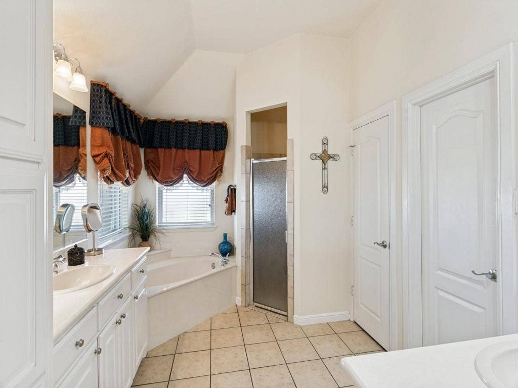 508 Singing Quail Trail, Haslet, TX 76052 Dual vanity with integrated sinks and white cabinetry, a built-in corner soaking tub, a tiled shower with a glass door, and neutral-toned floor tiling