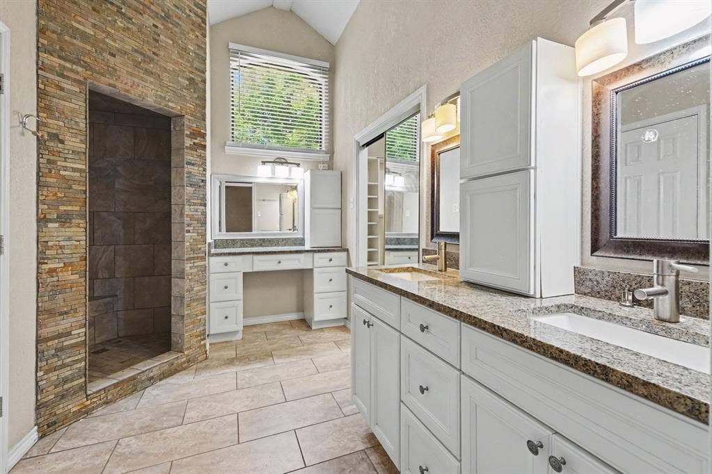 3313 Anchor Drive, Plano, TX 75023 Spacious bathroom featuring a stone-tiled walk-in shower, dual vanities with granite countertops, white cabinetry, and tiled flooring