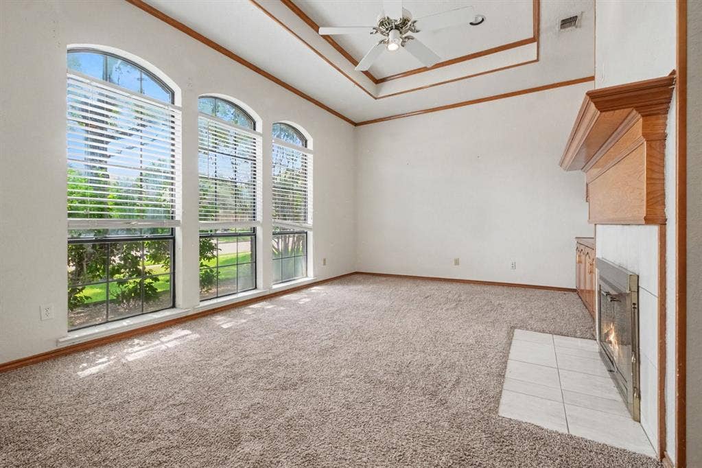 3313 Anchor Drive, Plano, TX 75023 Spacious room featuring three arched windows, a tray ceiling, and a fireplace with a wood mantel