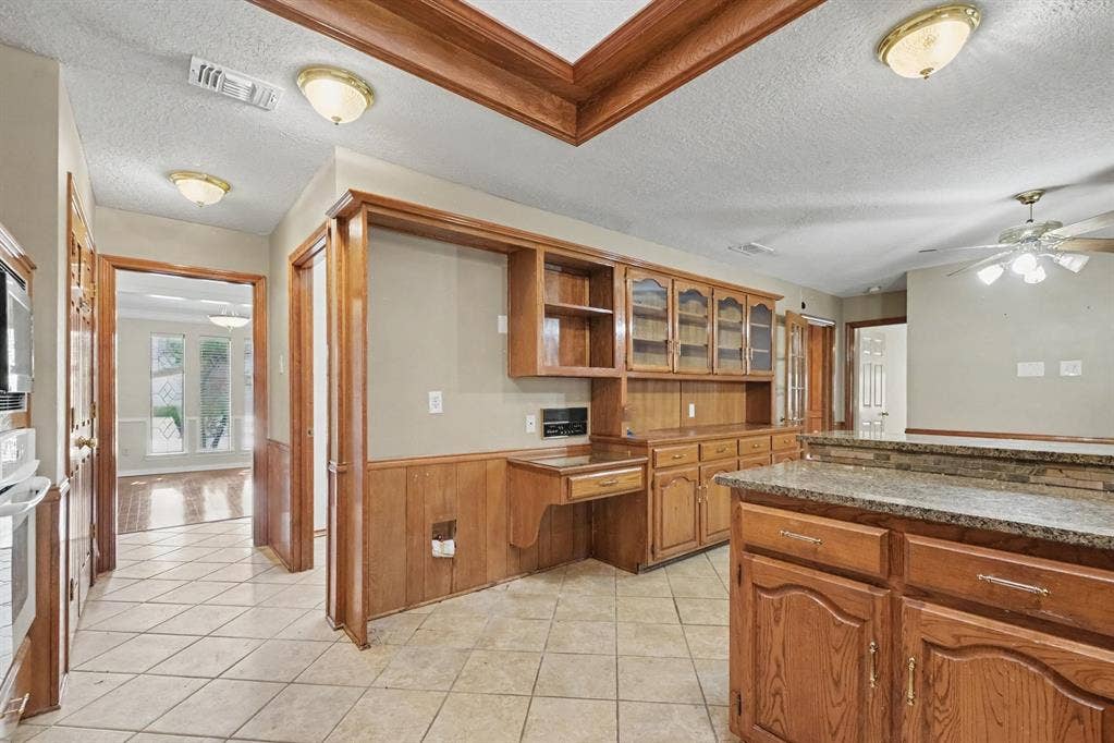 3313 Anchor Drive, Plano, TX 75023 Kitchen featuring wood-finish cabinetry, built-in desk, tile flooring, and a granite-style countertop