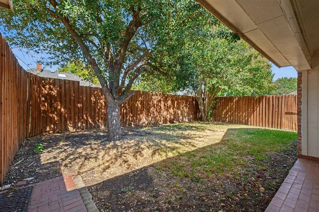 3313 Anchor Drive, Plano, TX 75023 Expansive outdoor space featuring a wood fence, mature tree, brick patio, and green lawn