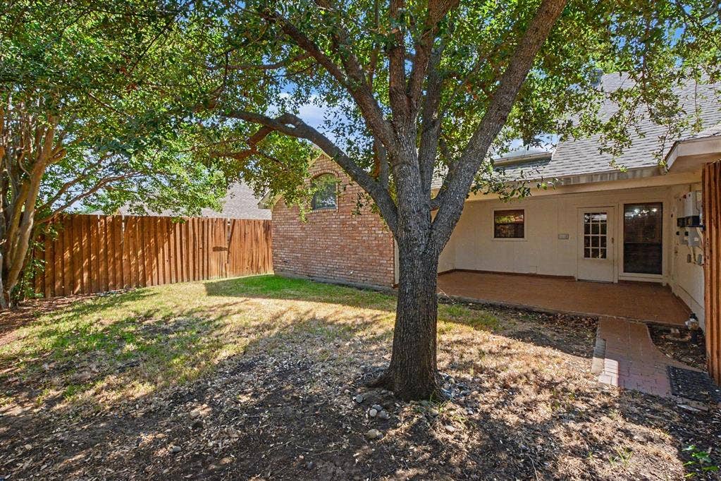 3313 Anchor Drive, Plano, TX 75023 Private backyard space with mature trees, a wooden privacy fence, a covered patio, and a brick pathway