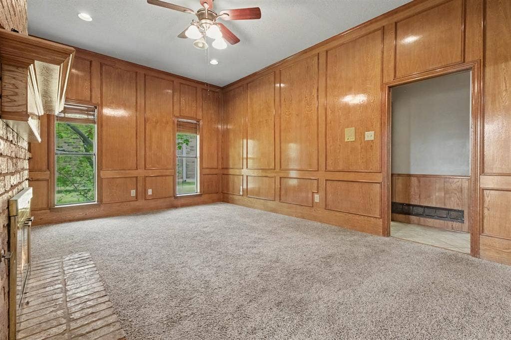 3313 Anchor Drive, Plano, TX 75023 Wood paneling with decorative trim, brick fireplace with mantel, ceiling fan with integrated lighting, and carpeted flooring