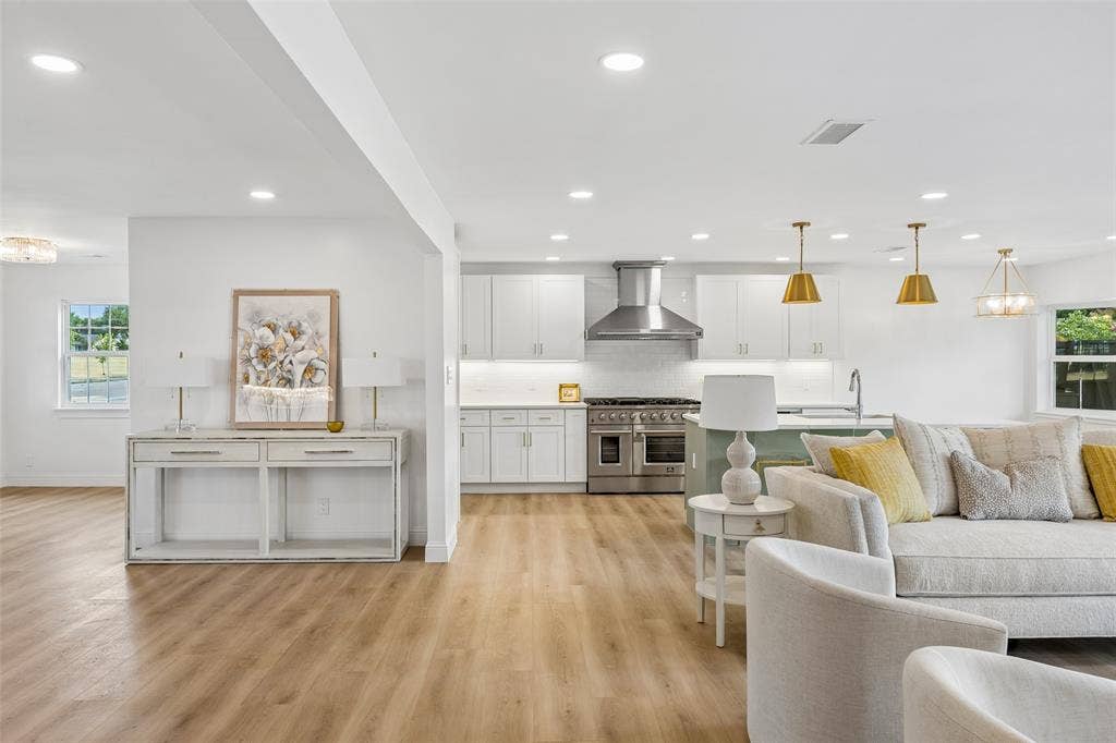 11864 Cold Harbor Lane, Dallas, TX 75244 Sunlit living and kitchen area featuring a professional range with brushed gold pendants and sleek white cabinetry.