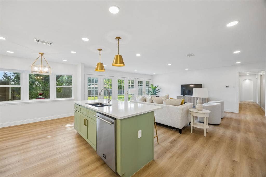 11864 Cold Harbor Lane, Dallas, TX 75244 Stylish kitchen island in sage green with quartz counters and brass pendants, opening directly into the adjoining living room.