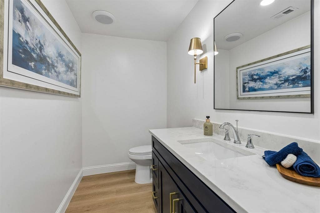 11864 Cold Harbor Lane, Dallas, TX 75244 Elegant powder bath with navy vanity, brushed gold hardware and sconces, and a sleek quartz countertop for a refined finishing touch.