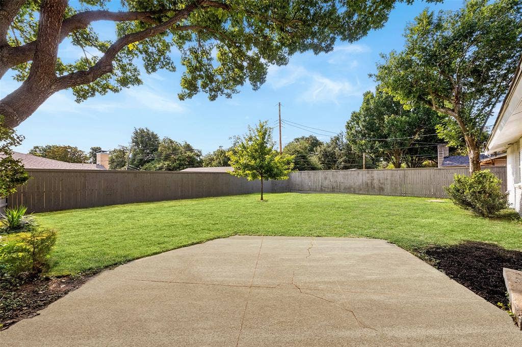 11864 Cold Harbor Lane, Dallas, TX 75244 Spacious backyard with mature shade tree framing a large open lawn, wood privacy fence, and a concrete patio ready for outdoor entertaining.