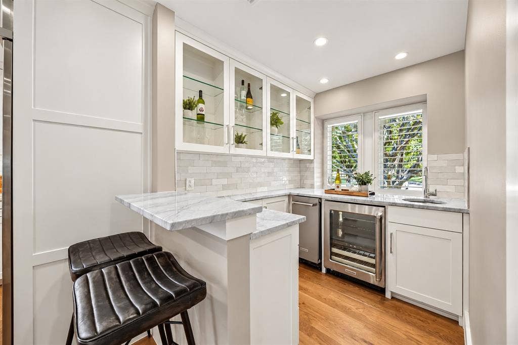 Custom cabinetry with glass-front display uppers, stone-surface bar area, integrated wine refrigerator, copper-like undermount sink, and ice machine for all your hosting needs.