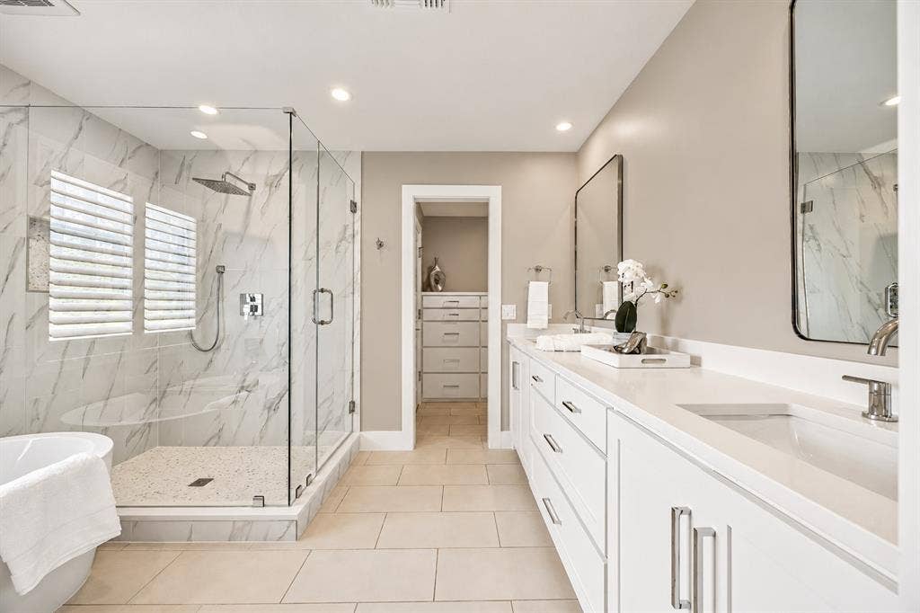 Dual-sink vanity with glass-enclosed walk-in shower, tile surround soaking tub, separate toilet space, two custom walk in closets, and magsafe hidden space